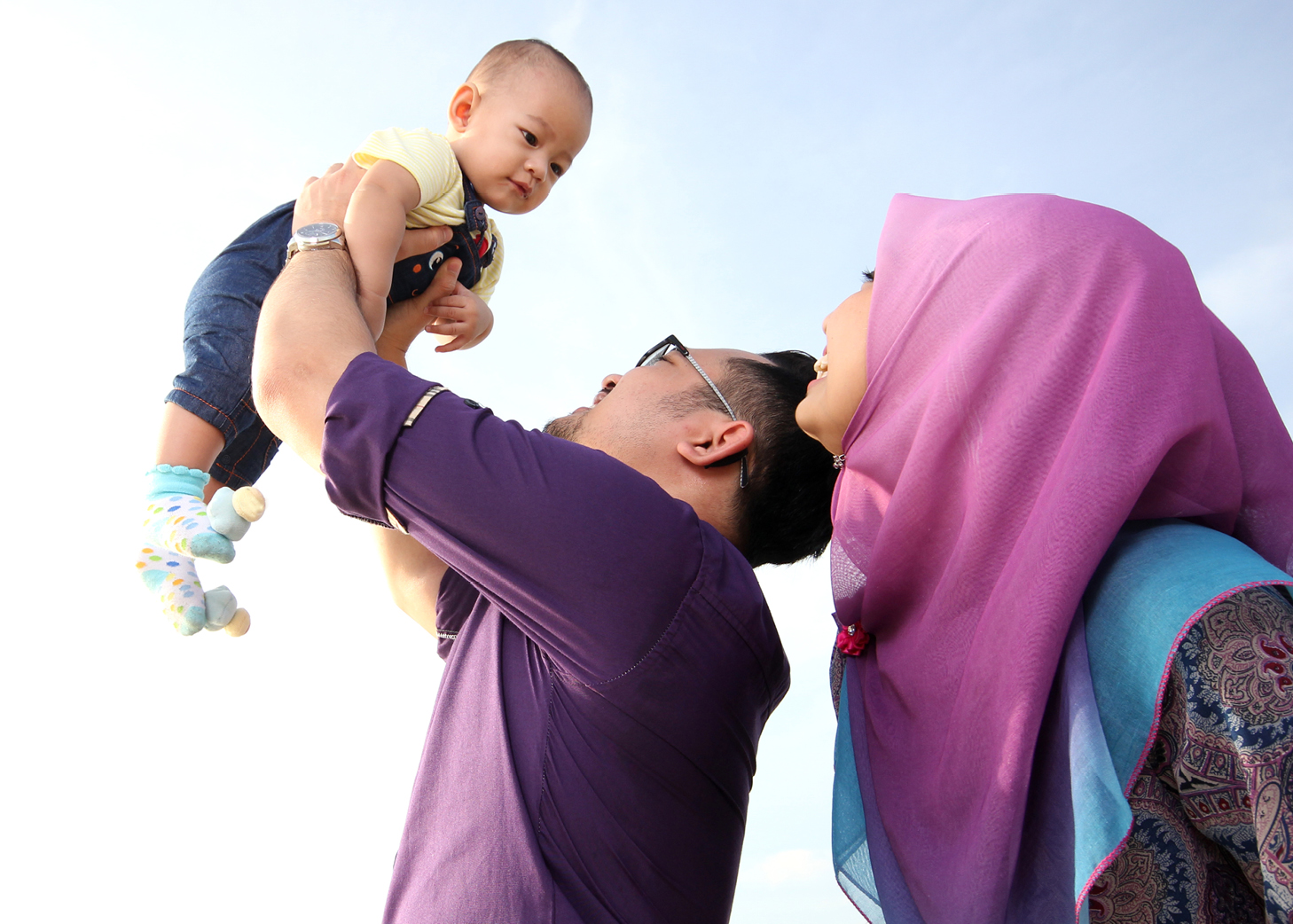 Asian father holding baby up in the air while mother looks on