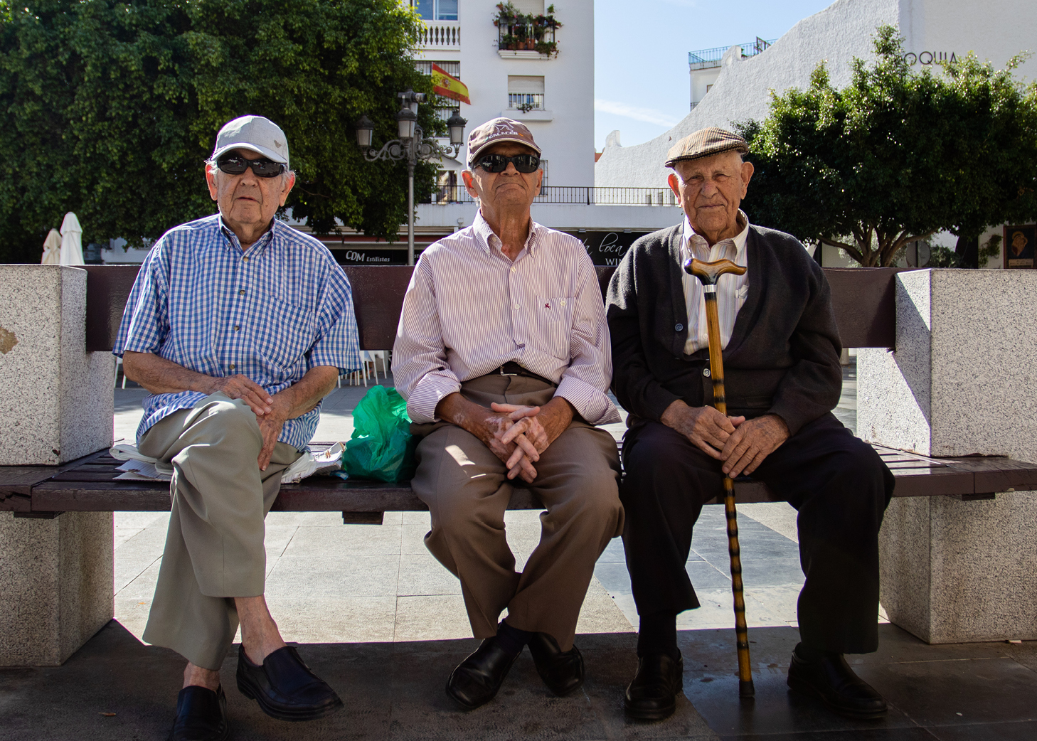 Three elderly men sitting on a bench in a town square