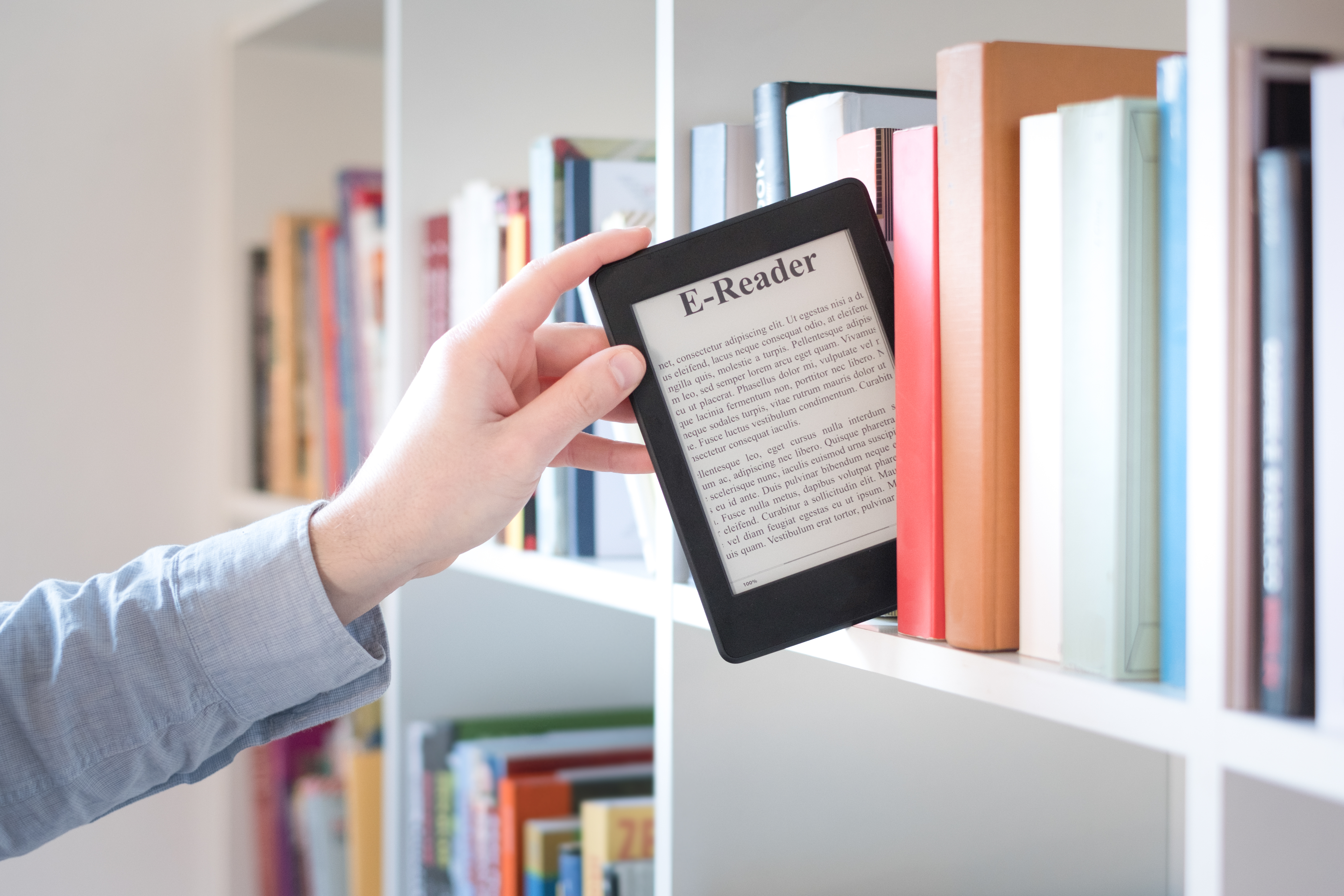 Hand reaching up to a library shelf pulling down an ereader